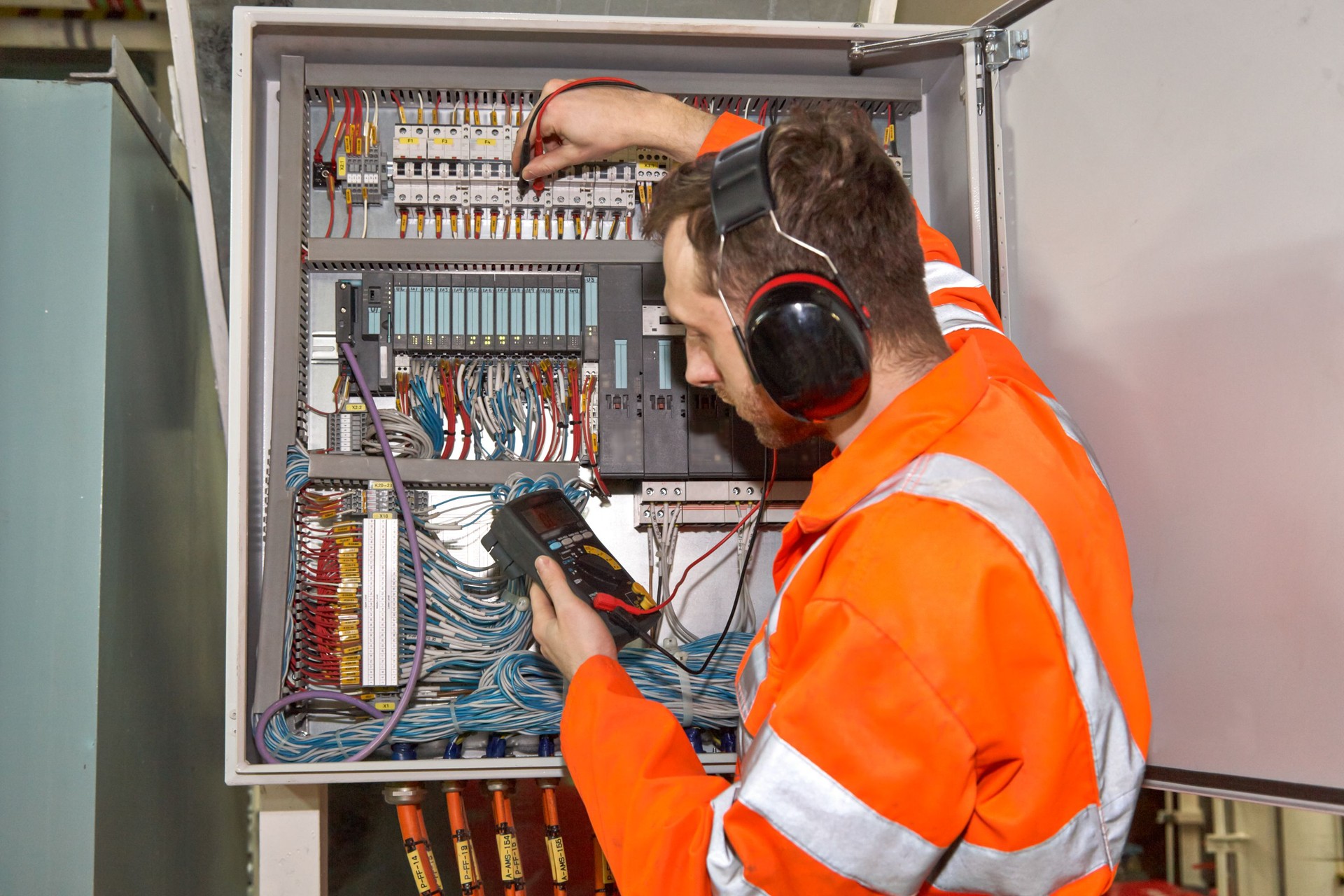 Offshore electrical engineer checking electrical controllers box with digital multi meter.